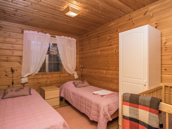 A wooden cabin room with two beds, a window with curtains, a wardrobe, and a small table. - Aurinkorinne by Interhome (Punkaharju)