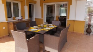 A dining area with a table set for four, surrounded by wicker chairs, and a view of the interior through a glass door.