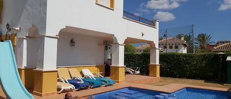 A pool area with lounge chairs and a person lying on a float.