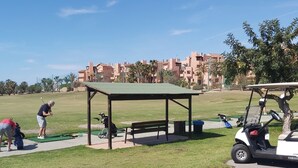 A golf course with a pavilion, a golf cart, and a person in a red shirt bending over.