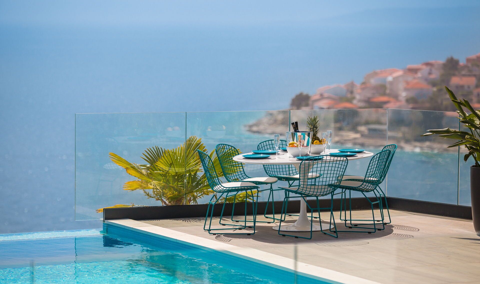 A dining area with a table and chairs, a pool, and a view of the sea.