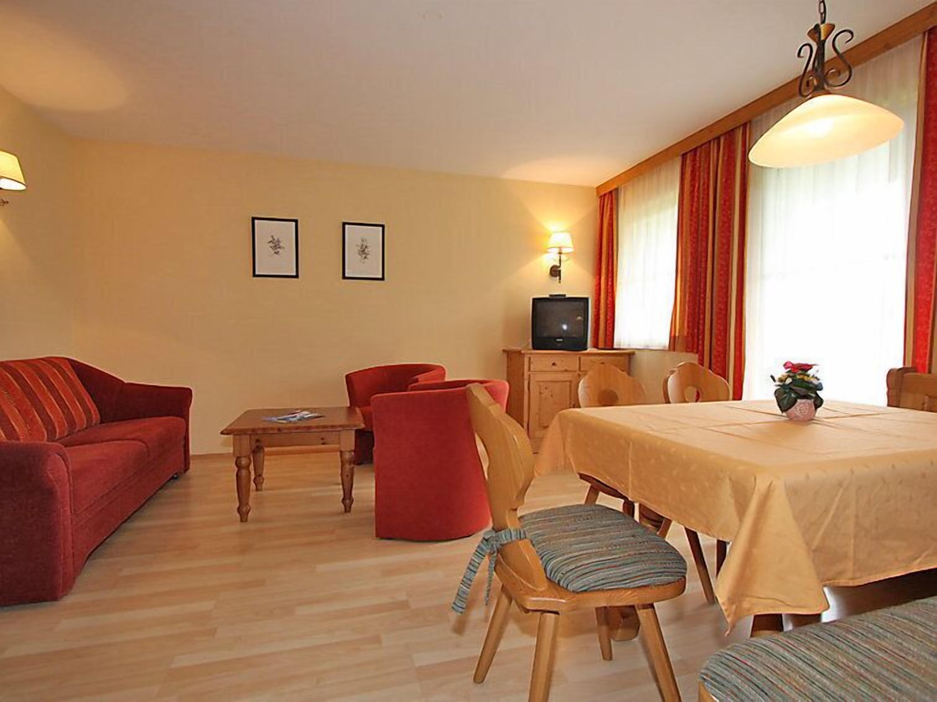 Ein gemütliches Zimmer mit einer roten Couch, einem Holzespeisetisch mit Stühlen, einem Fernseher und einem Fenster mit Vorhängen.