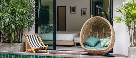 A modern pool area with a wicker chair, a striped lounge chair, and potted plants.