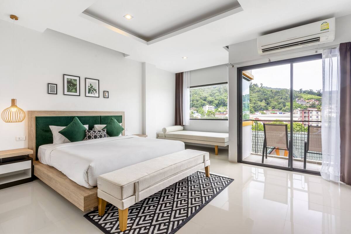 A modern hotel room with a large bed, a seating area by the window, and a balcony with a view of the city.