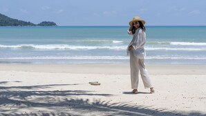 Eine Frau steht an einem Sandstrand, im Hintergrund das Meer.