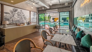 Ein Restaurant mit Blick auf einen Pool, Korbstühle und einem Neon-Schild.
