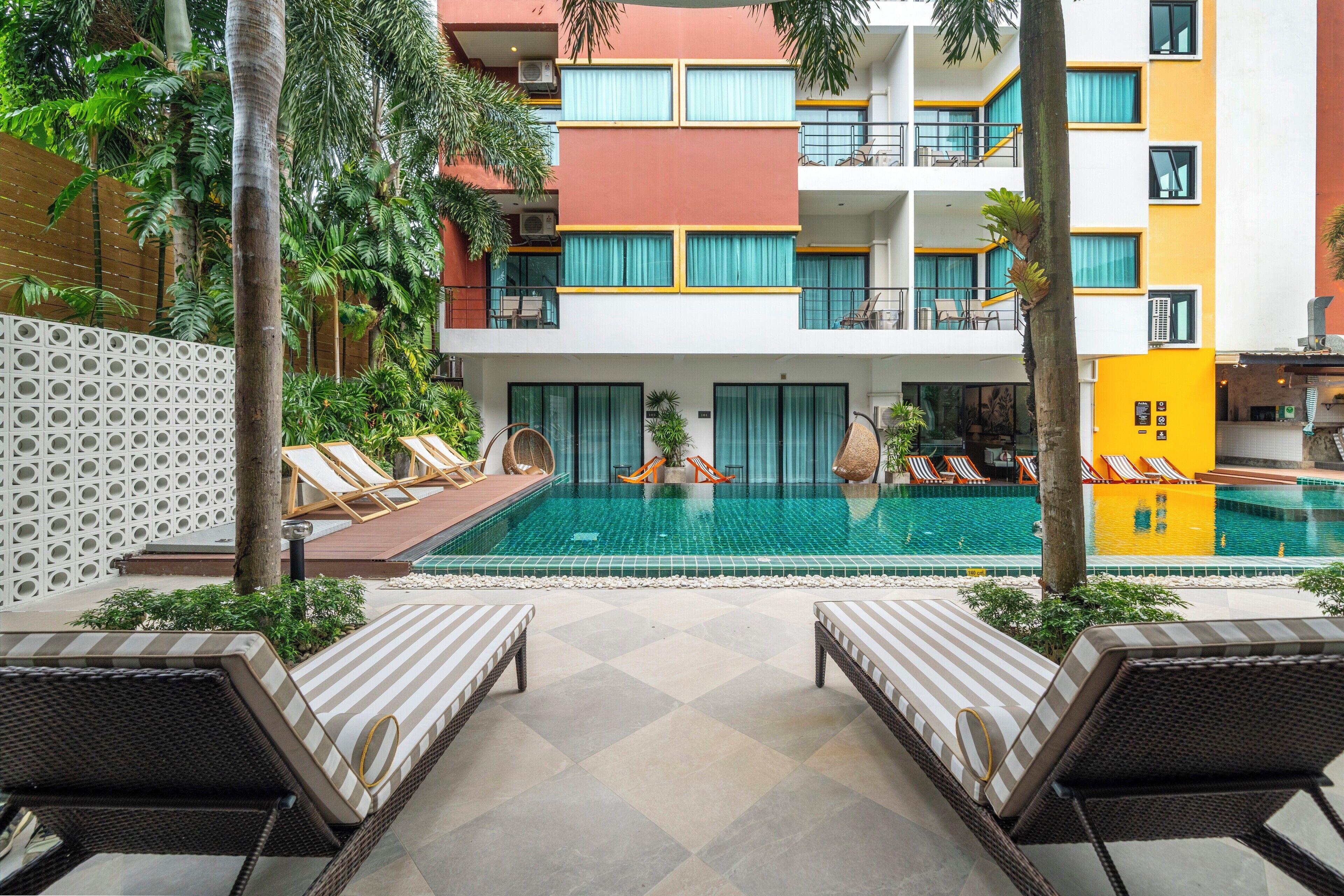 A hotel pool area with lounge chairs, a swimming pool, and a multi-story building with balconies.