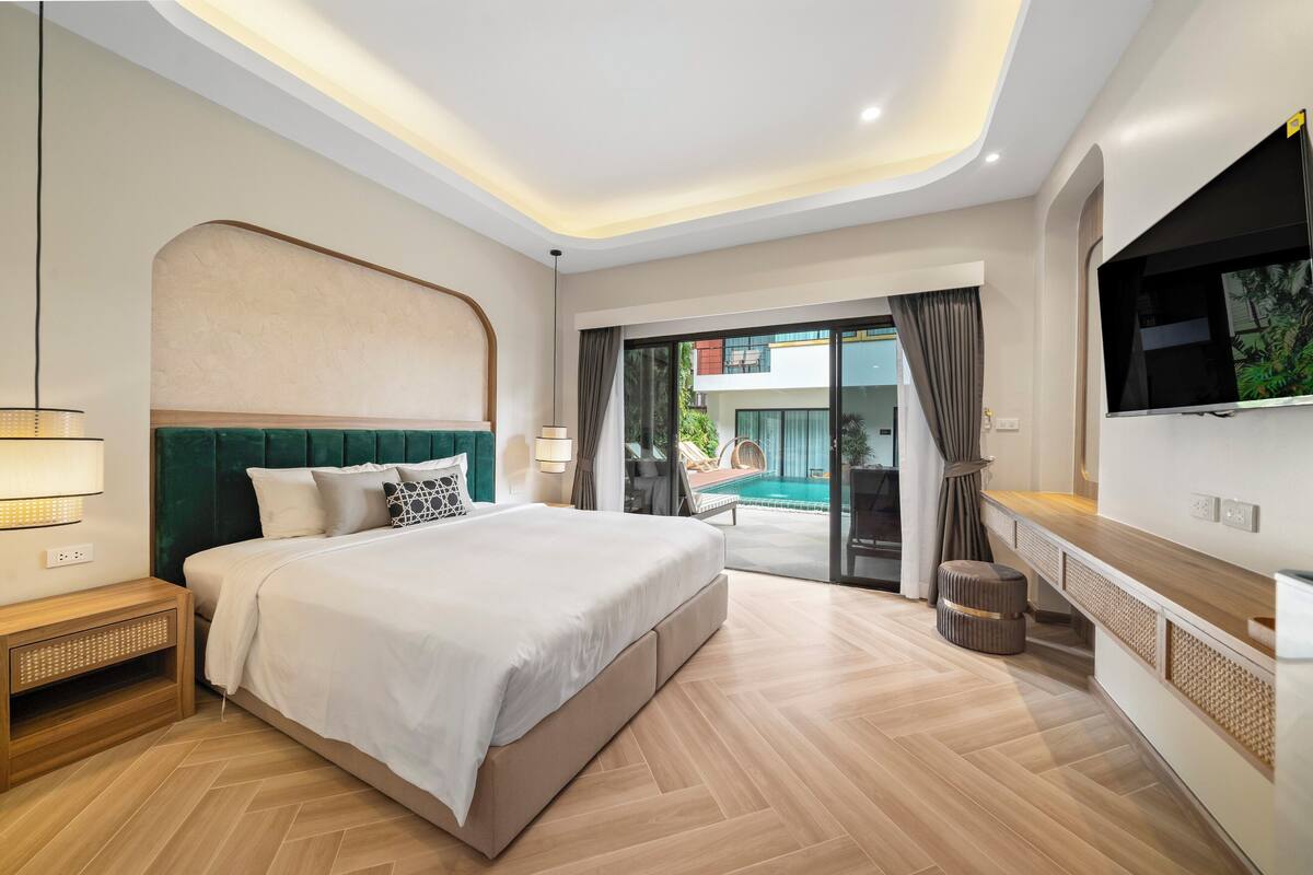 A modern hotel bedroom with a large bed, a TV, a wooden nightstand, and a view of a swimming pool.