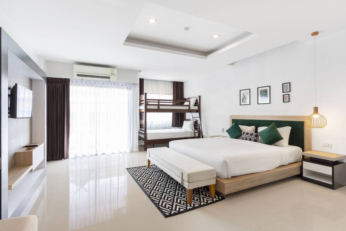 A modern hotel room with a large bed, a bench, a bedside table, and a TV.