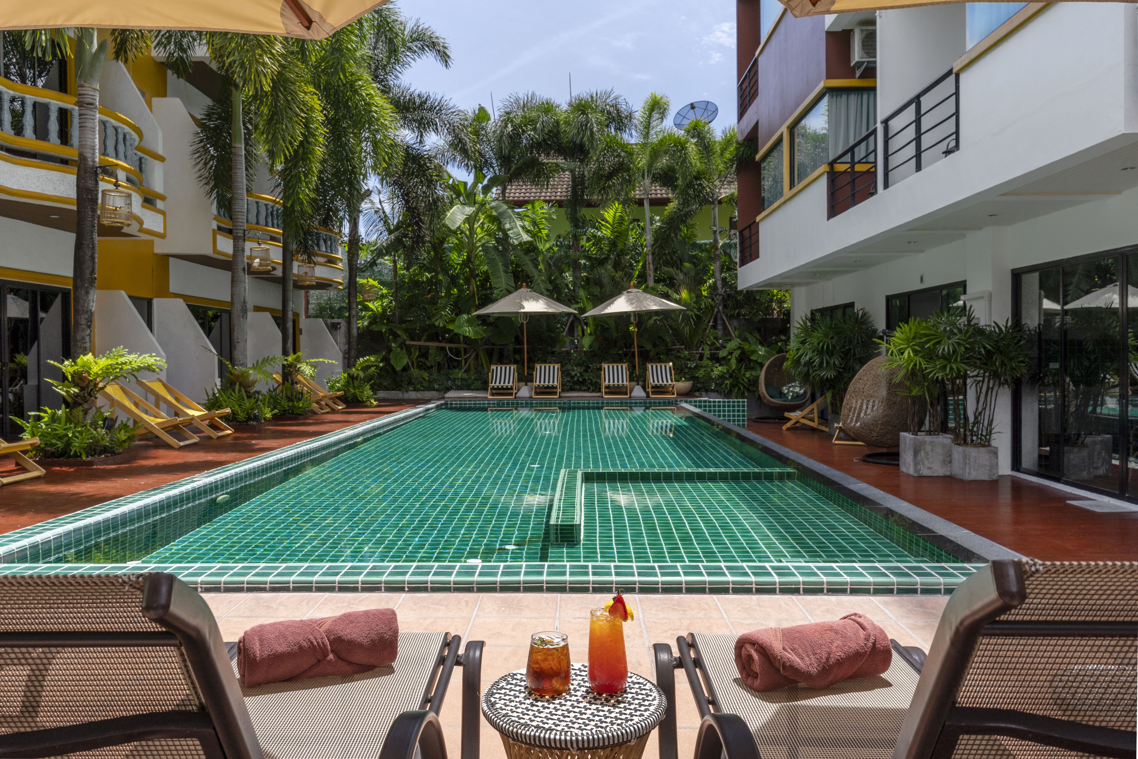 A swimming pool with lounge chairs and umbrellas, surrounded by greenery and modern architecture.
