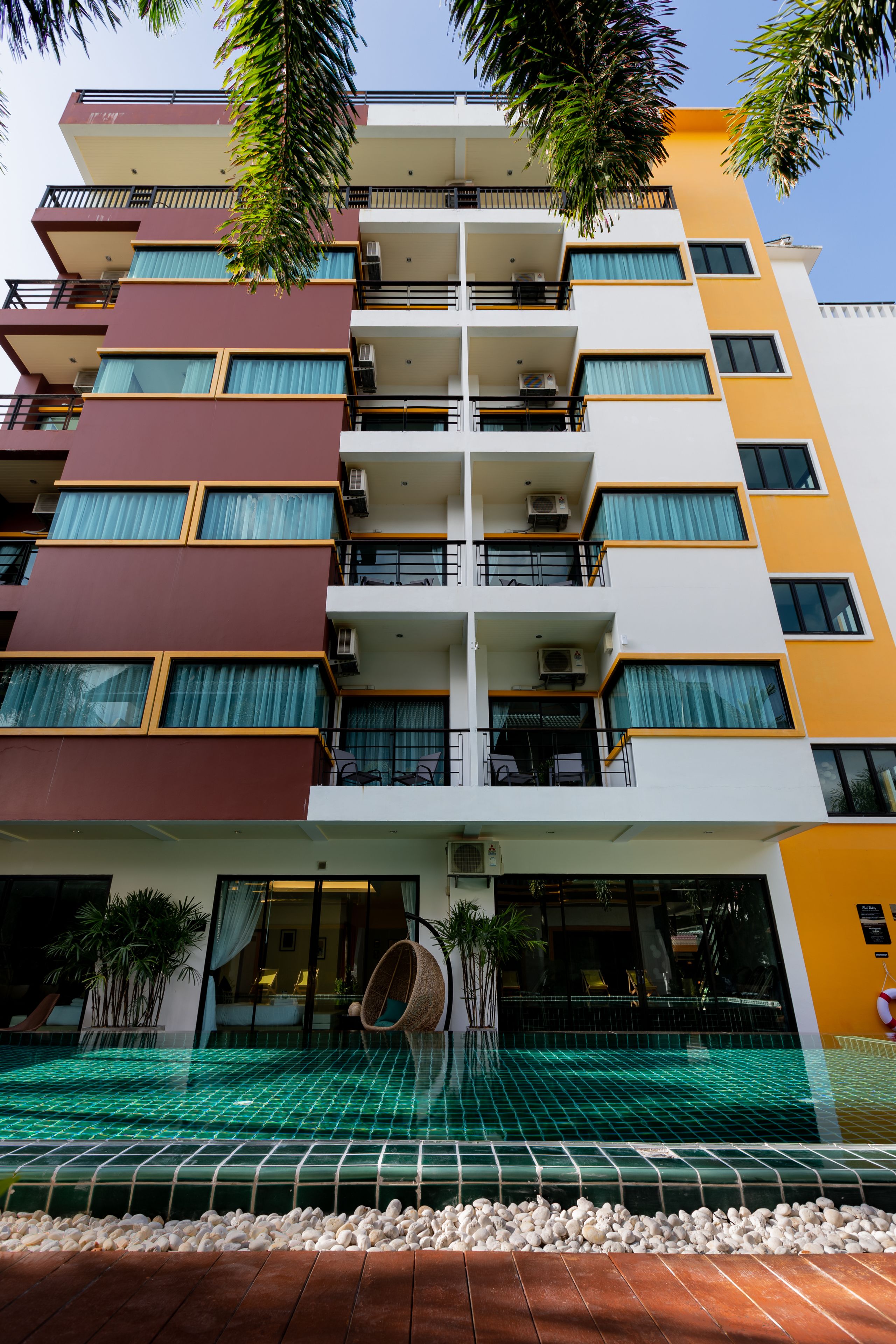 A multi-story hotel with balconies, a swimming pool, and a tiled entrance area.