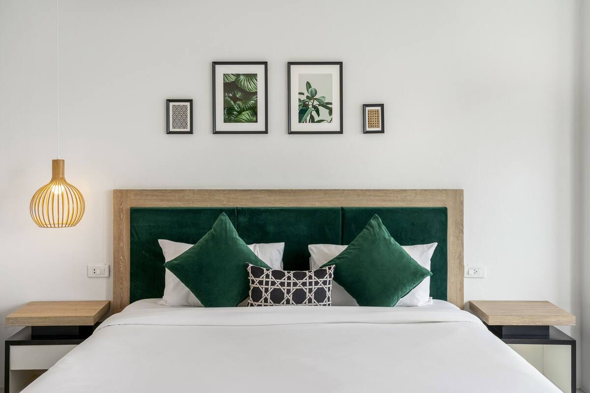 A neatly arranged bedroom with a wooden headboard, a bed with white bedding and green pillows, two bedside tables, and framed artwork on the wall.