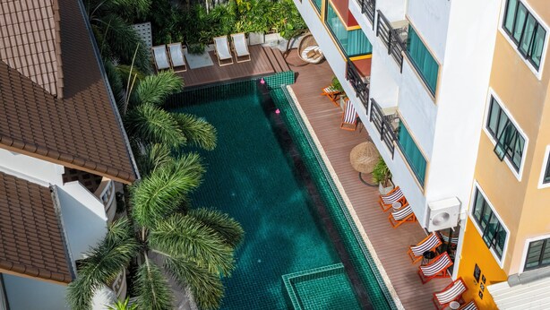 Eine Vogelperspektive auf ein Hotel mit einem Swimmingpool, umgeben von Palmen und Liegestühlen.