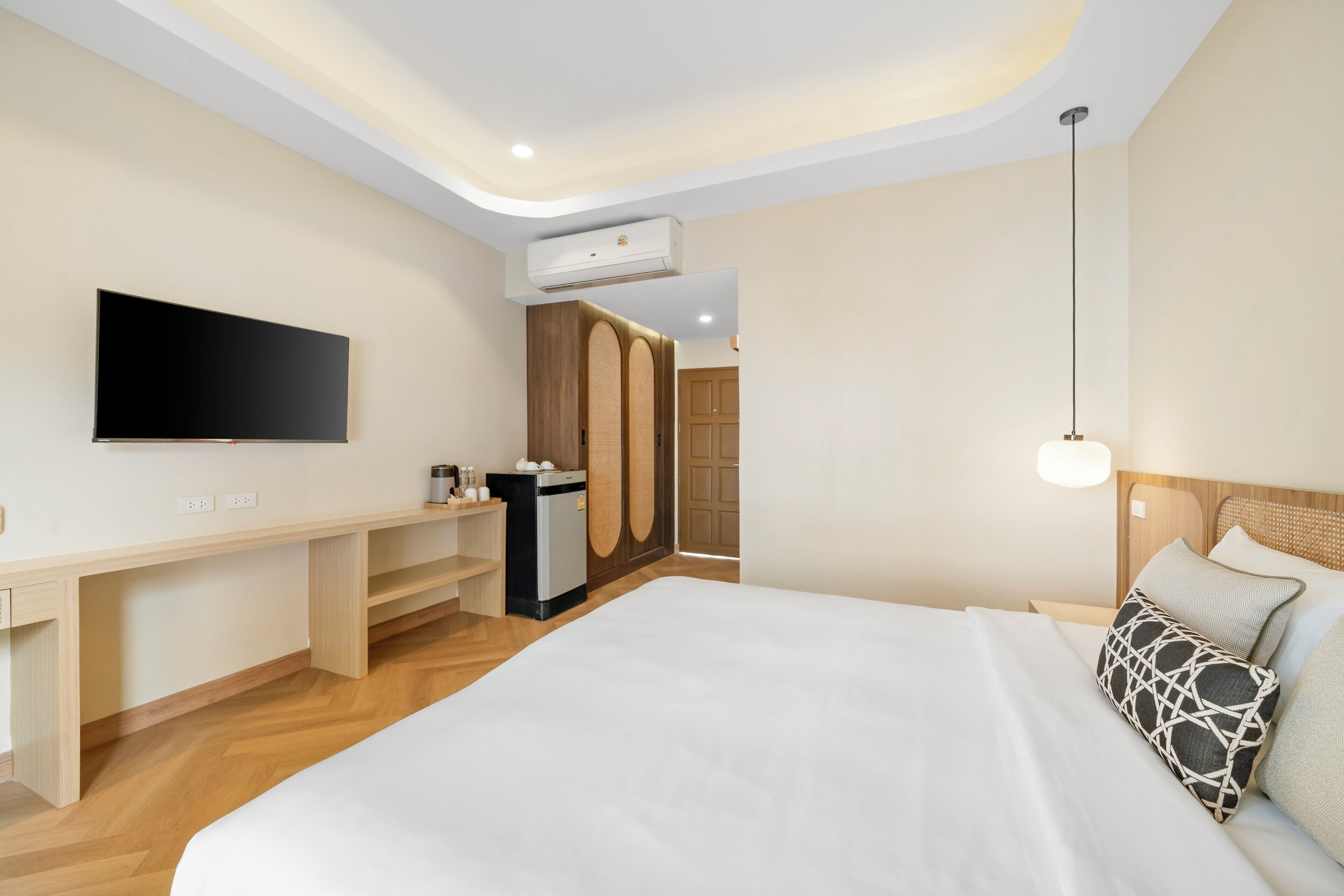 A modern hotel room with a large bed, a desk with a flat-screen TV, a wardrobe, and a bedside lamp.