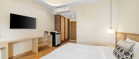 A modern hotel room with a large bed, a desk with a flat-screen TV, a wardrobe, and a bedside lamp.