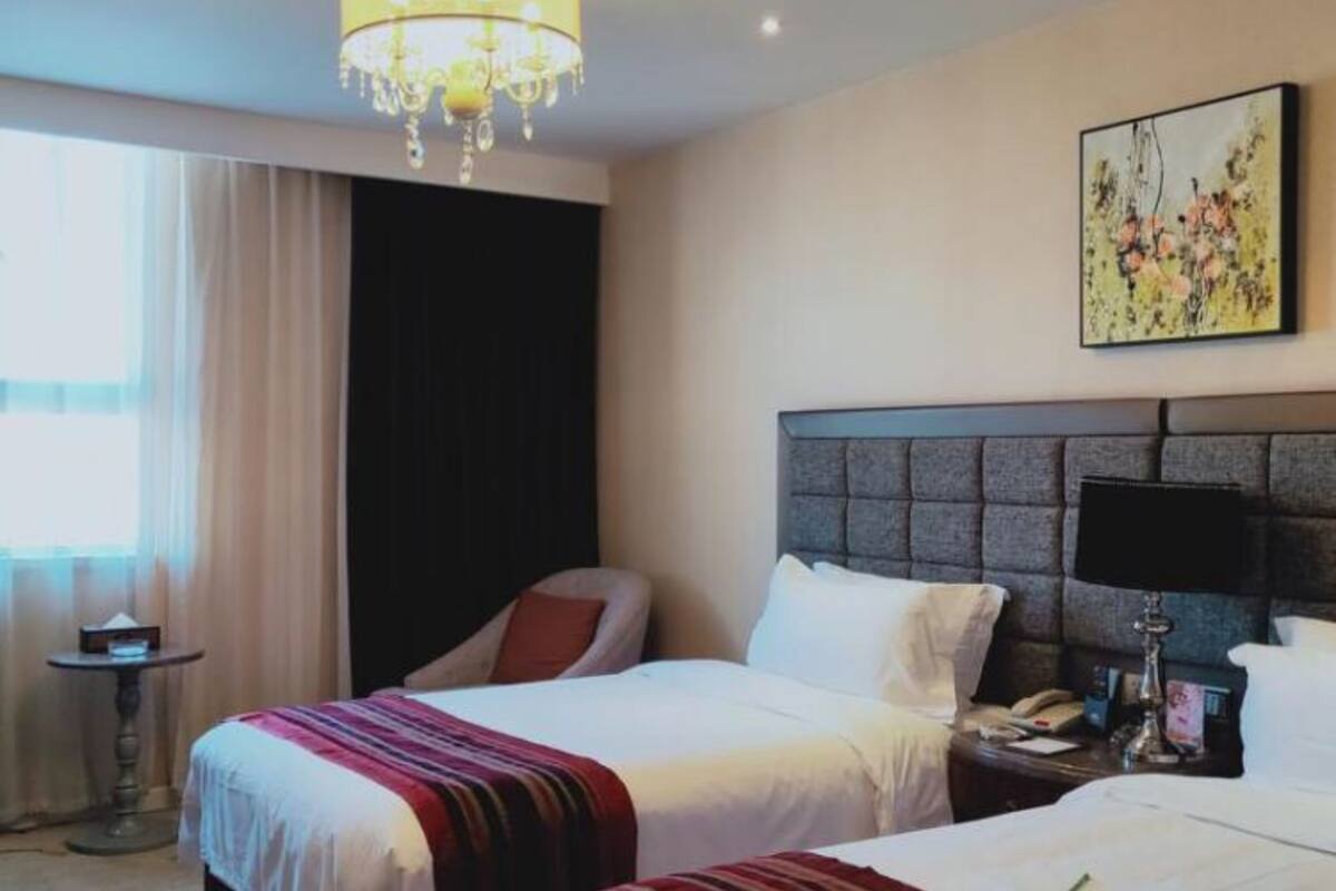 Une chambre d’hôtel avec deux lits, un lustre, un tableau et une petite table.