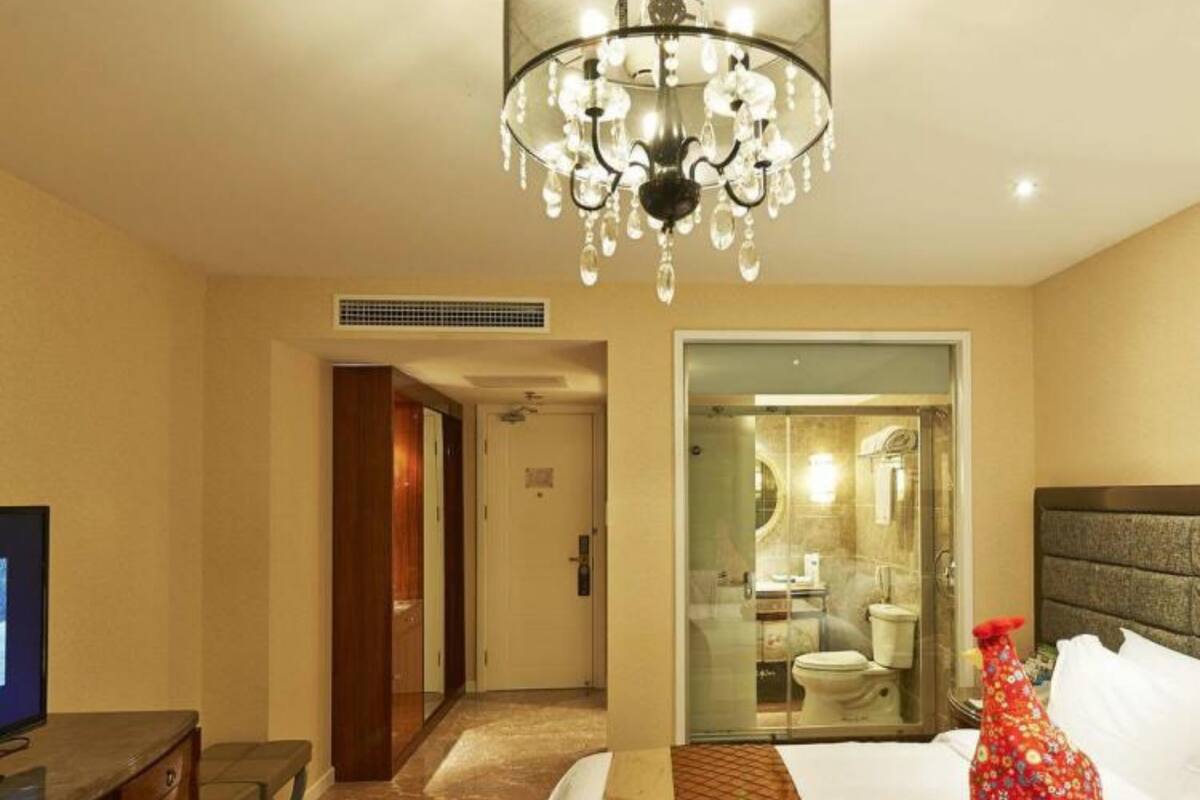 Une chambre d’hôtel équipée d’un lit, d’une télévision, d’un lustre et d’une salle de bain visible à travers une porte en verre.