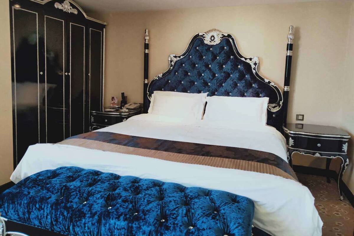 Un grand lit avec une tête de lit capitonnée, une table de chevet et une armoire.