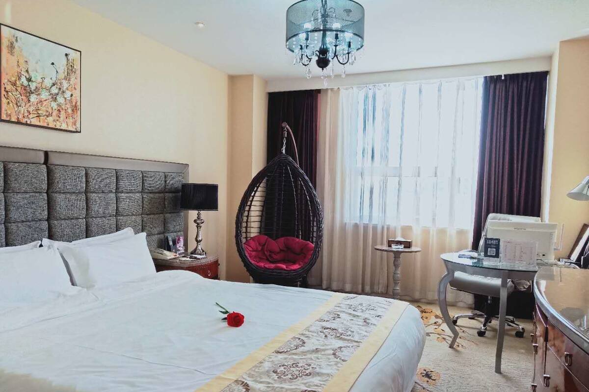 Une chambre d’hôtel avec un grand lit, un fauteuil suspendu, un bureau avec un ordinateur et un lustre.
