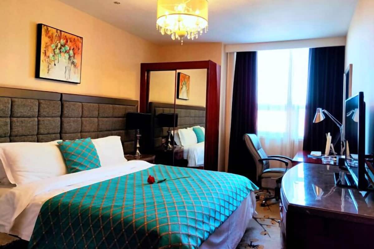 Une chambre d’hôtel avec un grand lit, un bureau avec un ordinateur, une chaise et un lustre.