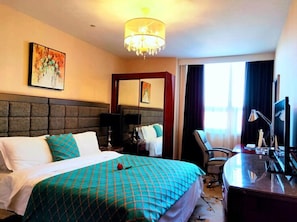 Een hotelkamer met een groot bed, een bureau met een computer, een stoel en een kroonluchter.