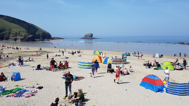 Uma praia com tendas, pessoas e um litoral rochoso.