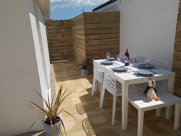 An outdoor dining area with a table set for four, potted plants, and a wooden fence in the background.