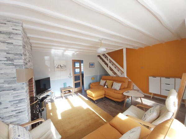 A spacious living room with a large sofa, a television, and a staircase leading to another level.
