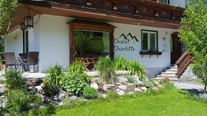 Una cabaña llamada 'Chalet Charlotte' con un balcón de madera, mobiliario exterior y un jardín.