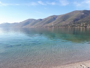 A clear lake with a pebbly shore and mountains in the background.