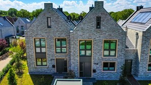Une maison moderne à deux étages, avec une façade en briques, de grandes fenêtres et un toit plat.