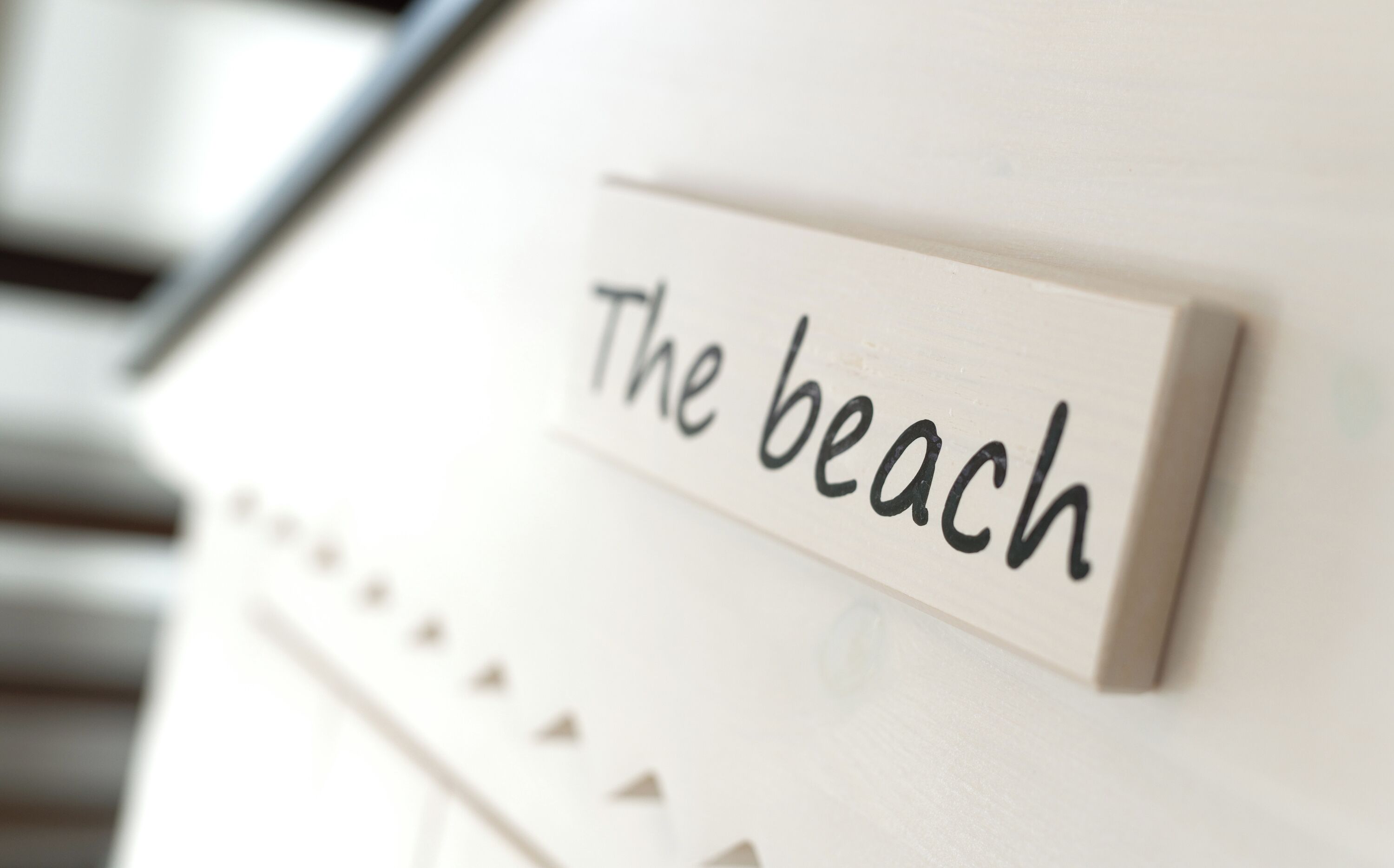 Ein Schild mit dem Schriftzug 'The beach' an einer weißen Wand.