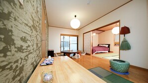 Ein traditioneller japanischer Raum mit Tatami-Bodenbelag, einem niedrigen Tisch mit einer gewebten Matte, einer grünen Zierurne und einer Schiebetür zu einem weiteren Raum.