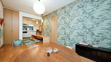 A dining area with a wooden table, a kitchen in the background, and a patterned wall.