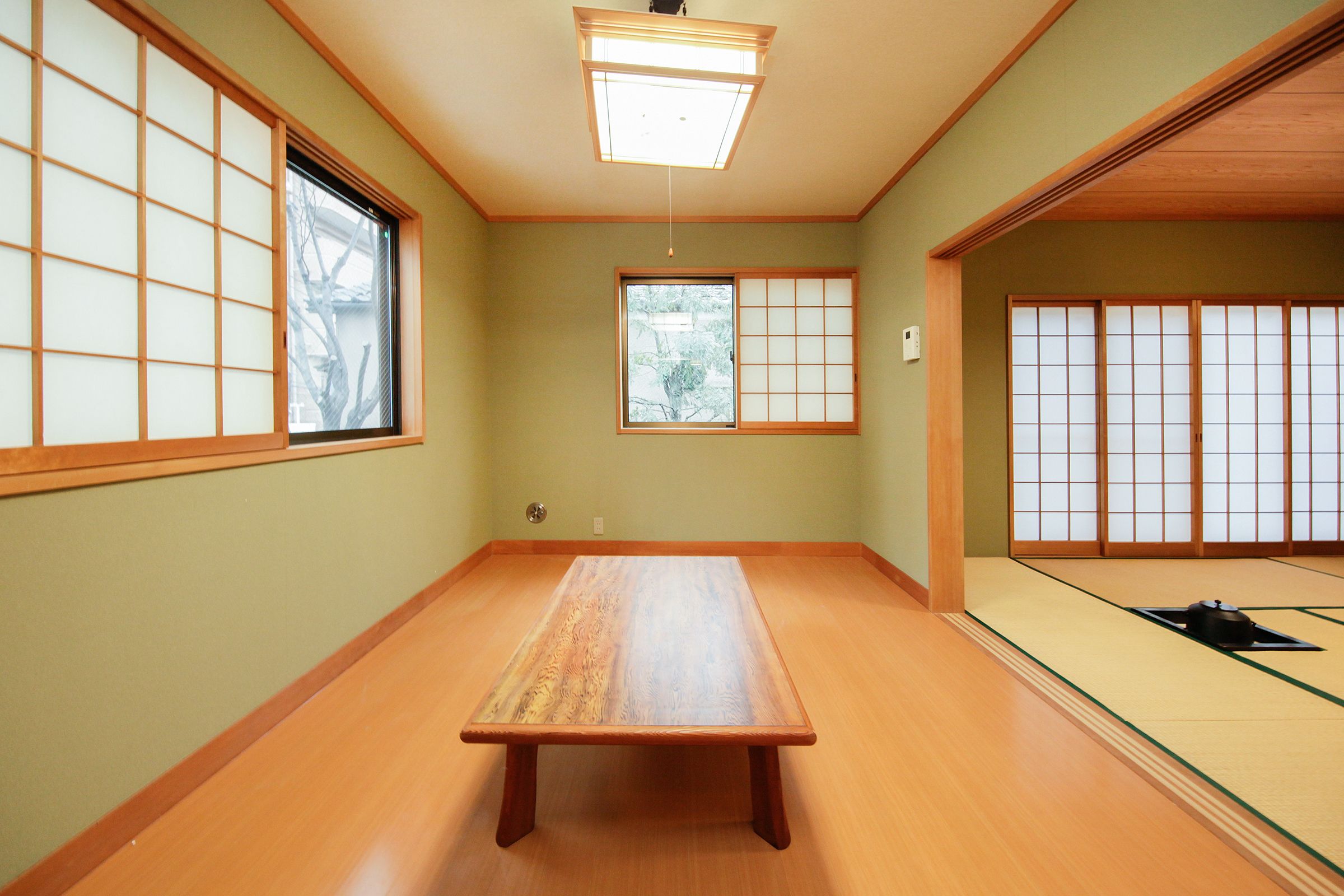 Une pièce de style japonais traditionnel, avec un sol recouvert de tatamis, une petite table en bois, des portes coulissantes en papier de riz (shoji) et un luminaire suspendu au plafond.