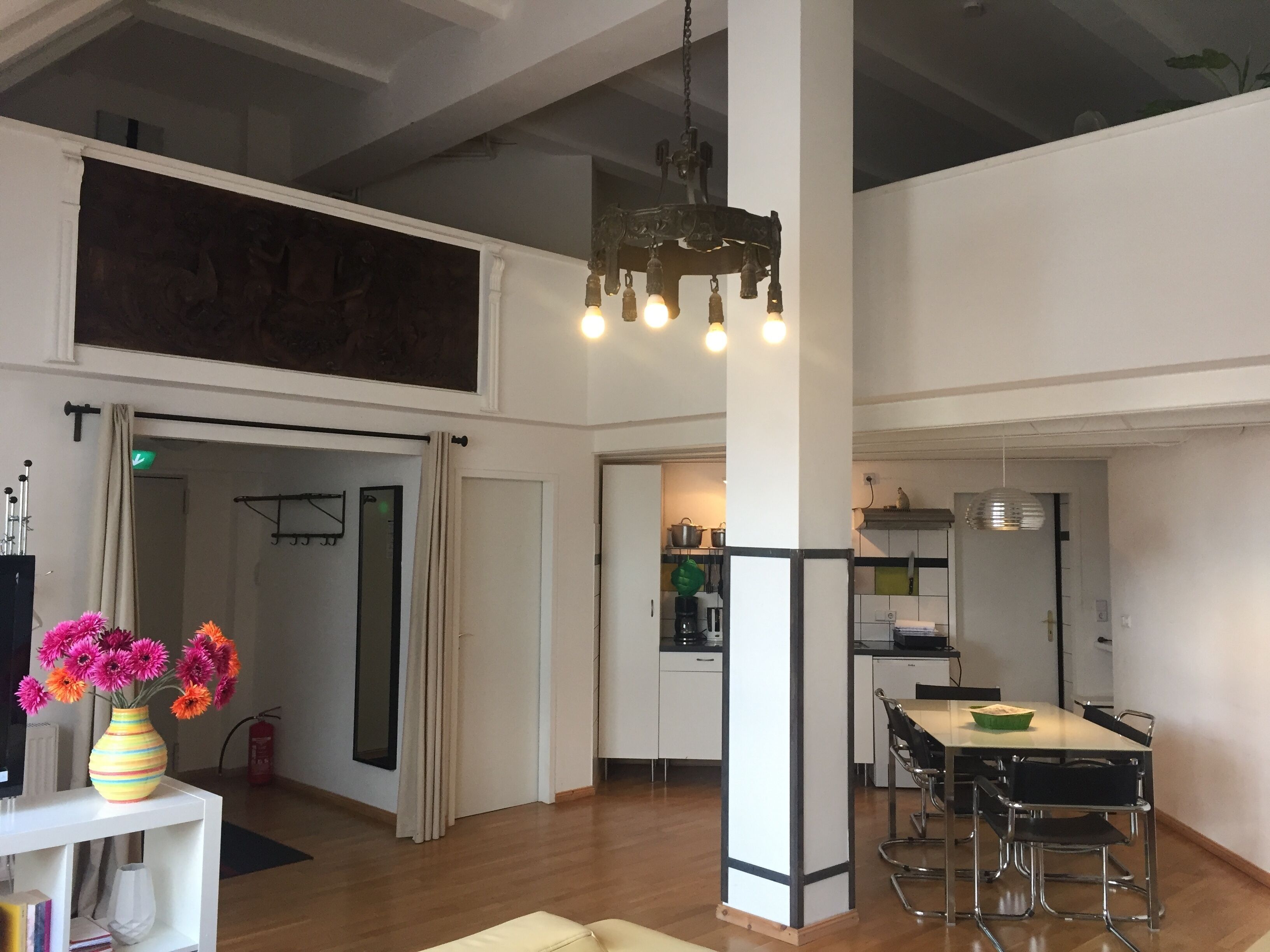 A spacious living area with a dining table, kitchen in the background, and a large window.