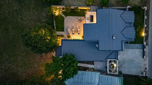 Eine Vogelperspektive zeigt ein Wohnhaus mit einer Steinterrasse, einem überdachten Sitzbereich im Freien und einer Garage.