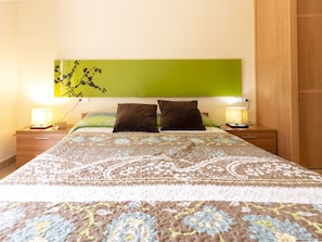 A neatly made bed with a patterned bedspread, two pillows, and two bedside lamps.