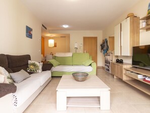 A living room with a brown sofa, a green sofa, a white sofa, a coffee table, and a TV stand with a flat-screen TV.