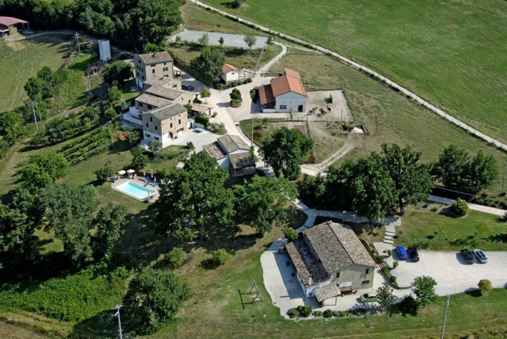 Oversigtsbillede af et boligområde med flere bygninger, en swimmingpool og en vej.