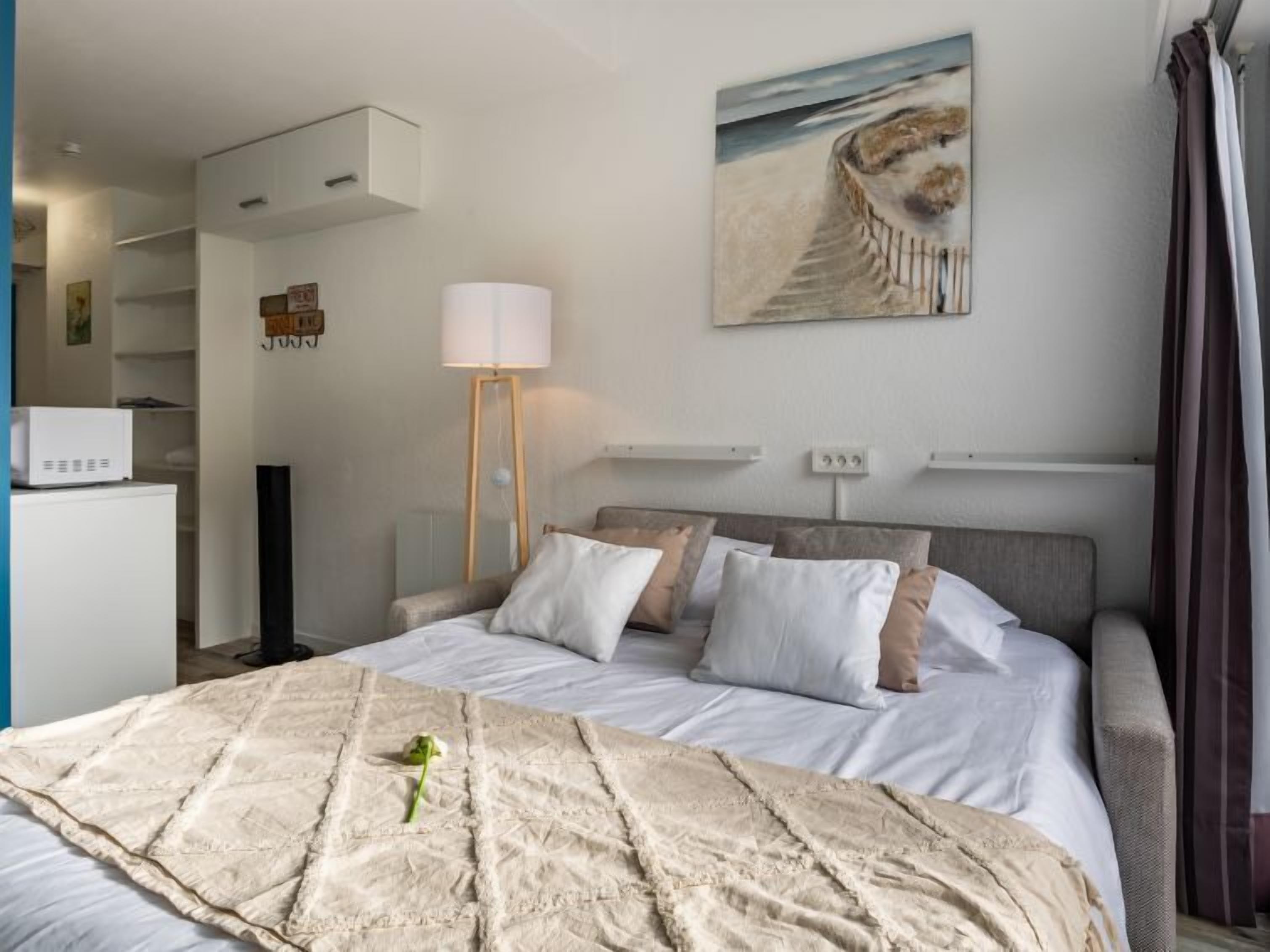 Une chambre d’hôtel avec un lit, une table de chevet, une lampe, un tableau et une vue sur la mer.