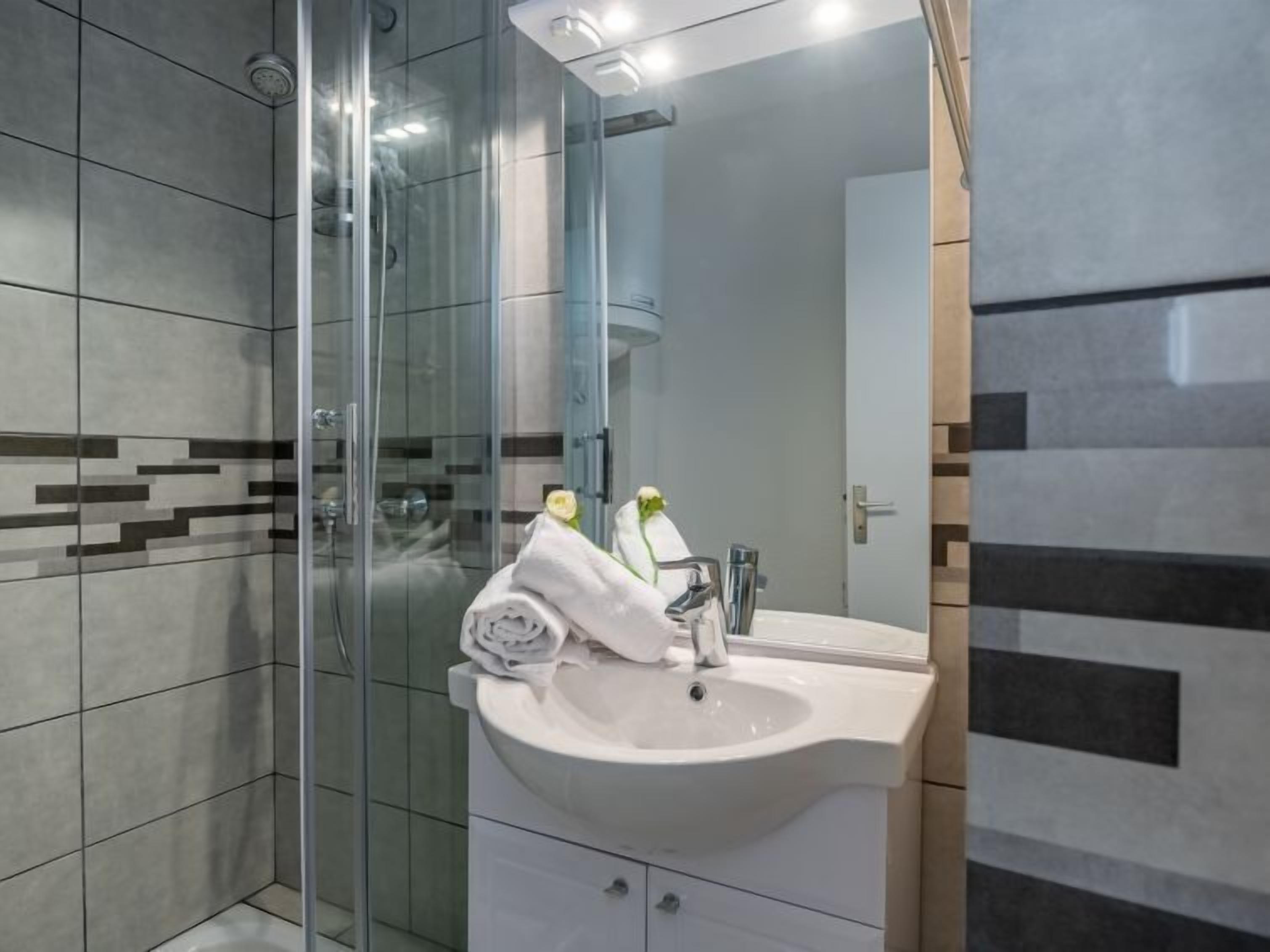 A modern bathroom with a glass shower enclosure, a white sink, and a mirror.