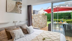Un dormitorio con una cama grande, una pared de piedra y un balcón de cristal con una sombrilla roja.