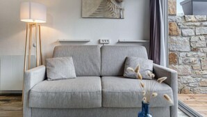 Una sala de estar moderna con un sofá gris, una lámpara de pie, un cuadro y una pared de piedra.