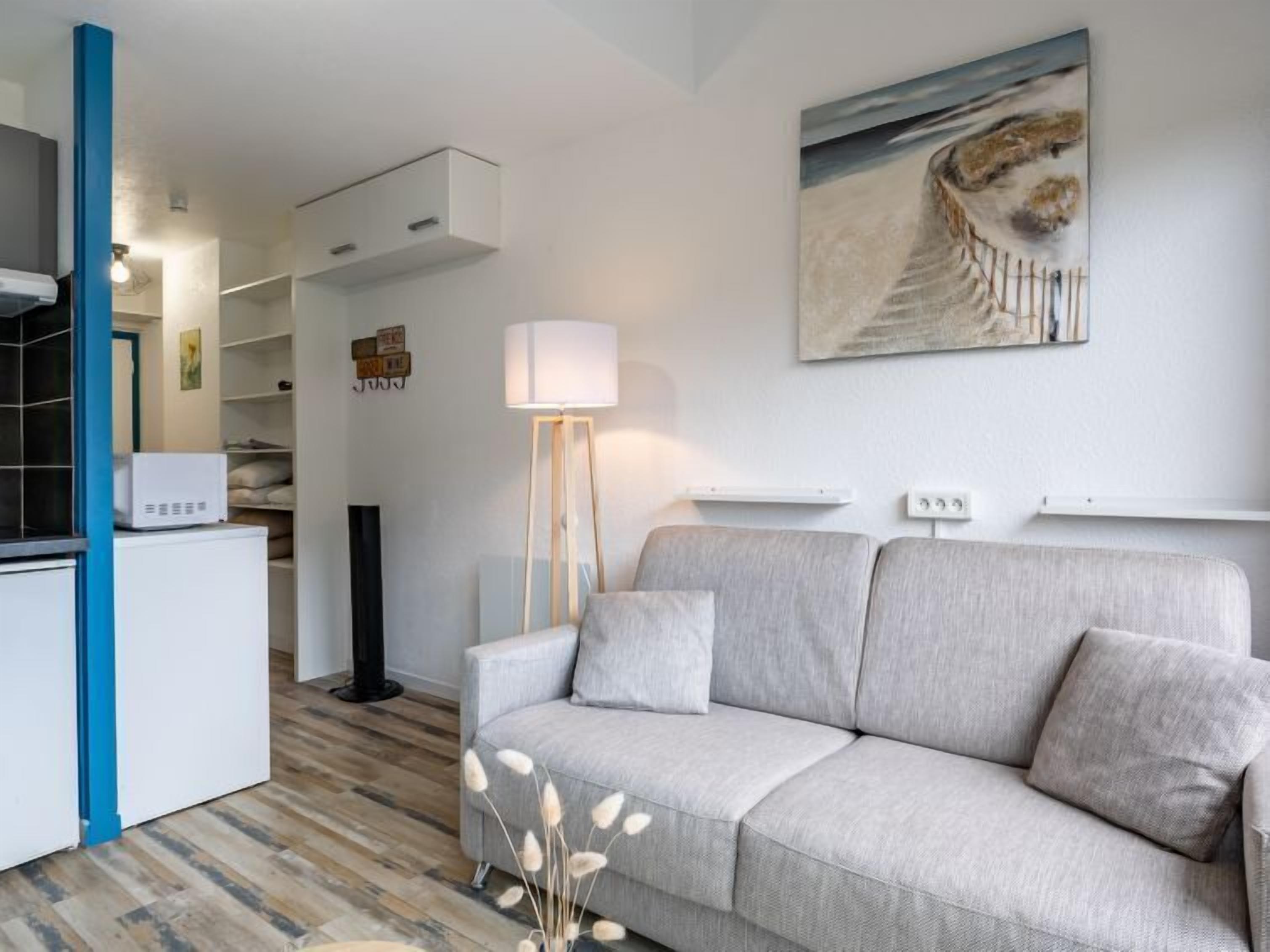Un salon moderne avec un canapé gris, une lampe sur pied et un tableau accroché au mur.