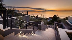 Eine moderne Treppe führt zu einem Balkon mit Blick auf ein Gewässer bei Sonnenuntergang.