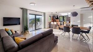 Ein modernes Wohnzimmer mit einer großen Couch, einem Essbereich mit Holztisch und Stühlen sowie einer Küche im Hintergrund.