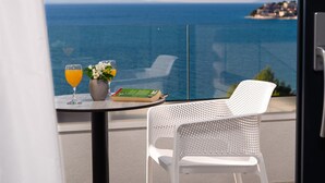 Ein Balkon mit Tisch, einem weißen Stuhl, einem Buch, einer Blumenvase und zwei Gläsern Orangensaft.