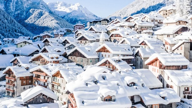 En snötäckt by med traditionella trähus, med berg som majestätisk bakgrund.