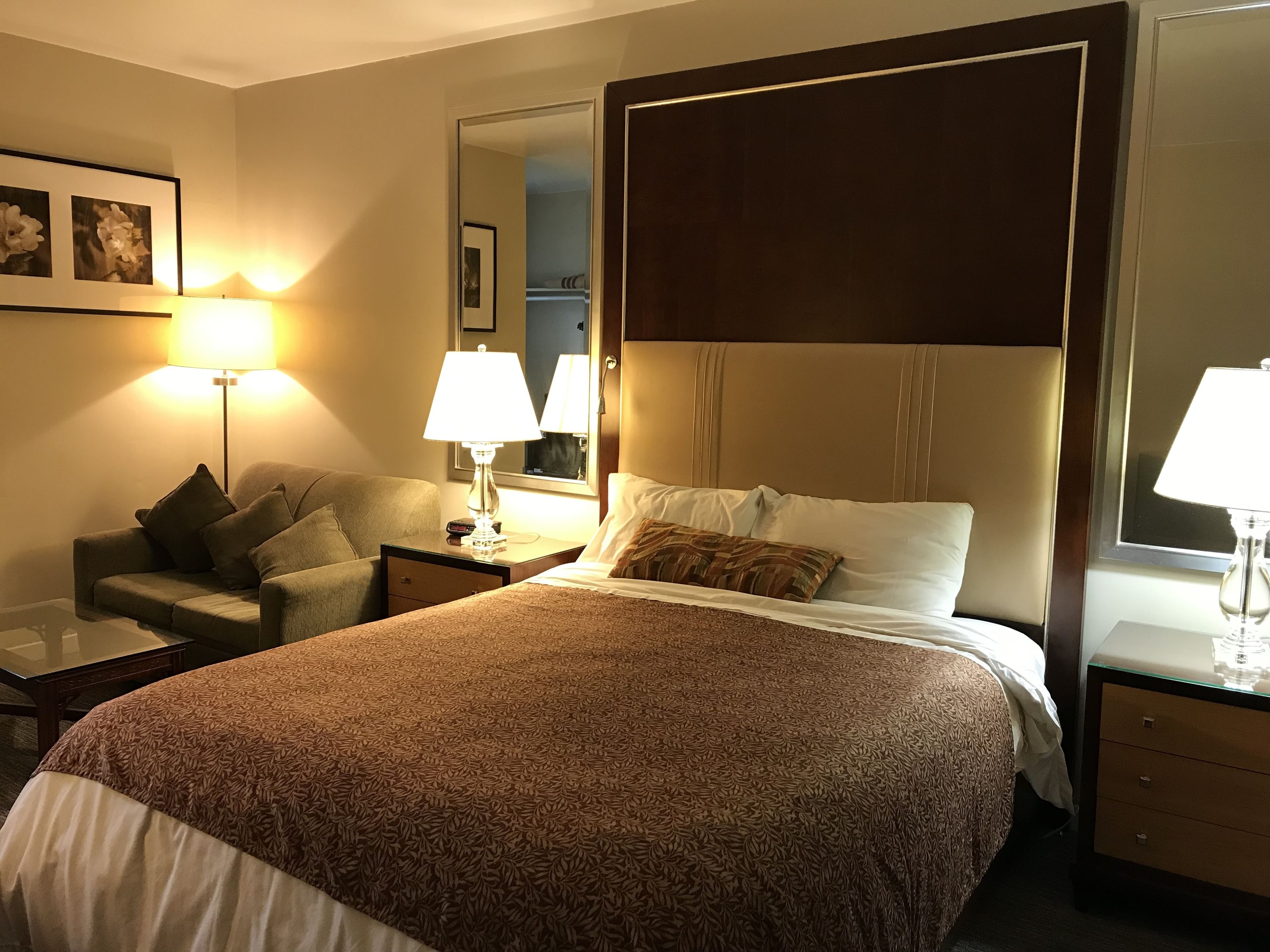 A hotel room with a large bed, a sofa, a desk, and a mirror.